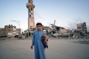 TOPSHOT - A Palestinian boy carrying his prayer mat, poses for a picture before joining the morning the Eid al-Adha prayer in Khan Yunis in the southern Gaza Strip, on the first day of the Muslim holiday marking the end of the hajj pilgrimage to Mecca, on June 16, 2024. (Photo by Bashar TALEB / AFP)